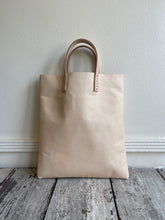 Load image into Gallery viewer, natural vegetable tanned leather bags small size, narrow-rectangular flat shape. two veg tan handles attached/sewn using belgian linen yarn. also made in distressed brown & black leather and black & tan suede. Retail price $195.