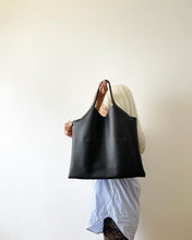 Load image into Gallery viewer, bag with short handle and a short v shaped dip at the center of the bag. the black leather used looks supple.