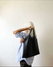 Load image into Gallery viewer, bag with short handle and a short v shaped dip at the center of the bag. the black leather used looks supple.