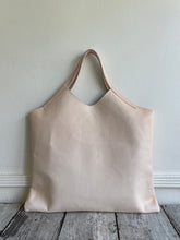 Load image into Gallery viewer, sitting on a table is a bag with short handles and a short v shaped dip at the center of the bag made in a natural veg tan leather. no patina yet.