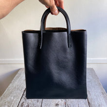 Load image into Gallery viewer, Black and brown leather bags small size, narrow-rectangular flat shape. two veg tan handles attached/sewn using belgian linen yarn. also made in natural vegetable tanned leather and black & tan suede. Retail price $195.