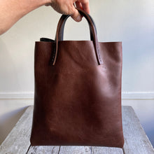 Load image into Gallery viewer, Black and brown leather bags small size, narrow-rectangular flat shape. two veg tan handles attached/sewn using belgian linen yarn. also made in natural vegetable tanned leather and black & tan suede. Retail price $195.