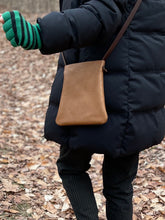Load image into Gallery viewer, woman stands wearing x-small tan leather crossbody bag. its bottom corners are rounded.
