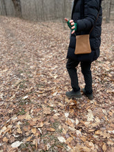 Load image into Gallery viewer, woman stands wearing x-small tan leather crossbody bag. its bottom corners are rounded. This bag is artisan made and handcrafted.