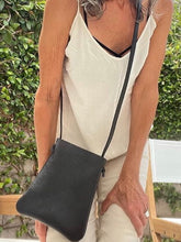 Load image into Gallery viewer, woman stands wearing x-small black leather crossbody bag. its bottom corners are rounded. This bag is artisan made and handcrafted.