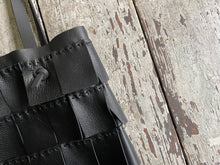 Load image into Gallery viewer, A close up of a black leather bag with three rows of wide black leather hand sewn fringe covering 1/3 of the small-size bag starting at the top lays flat on a table top its shoulder.