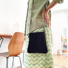 Load image into Gallery viewer, woman stands wearing x-small black suede bag its bottom corners are rounded. strap length can be worn crossbody. This bag is artisan made and handcrafted.
