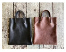 Load image into Gallery viewer, Black and brown leather bags small size, narrow-rectangular flat shape. two veg tan handles attached/sewn using belgian linen yarn. also made in natural vegetable tanned leather and black & tan suede. Retail price $195.